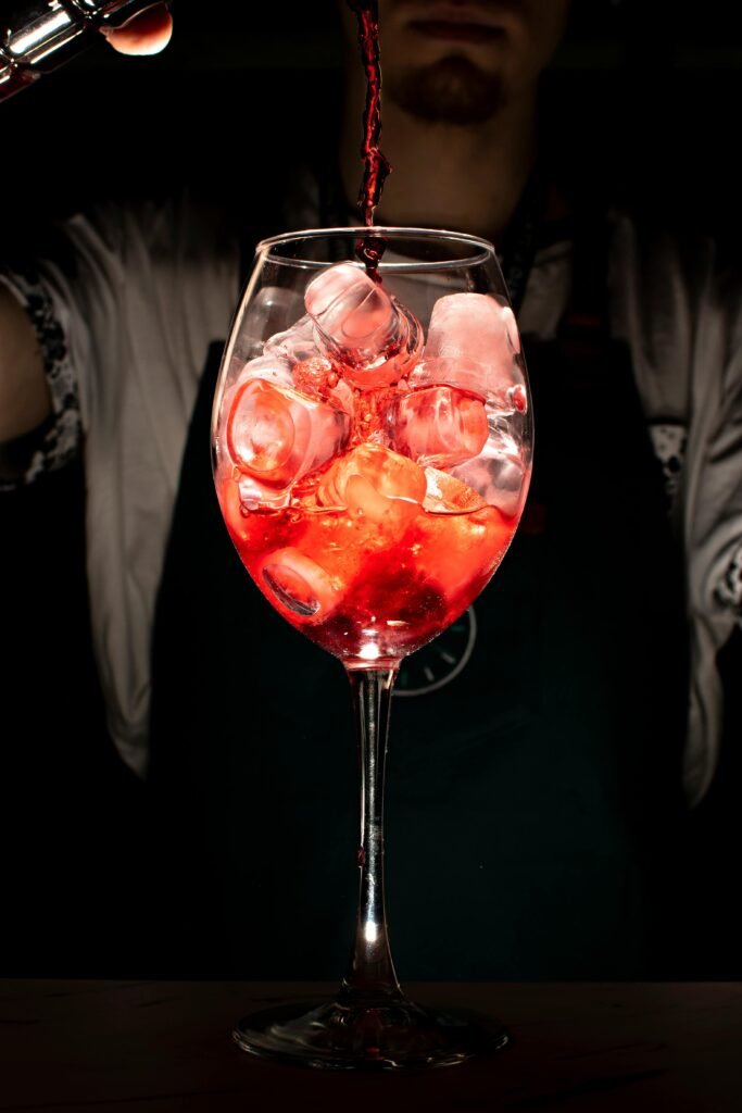 Vibrant cocktail pour into an ice-filled wine glass by a bartender, highlighting the drink's color and texture.
